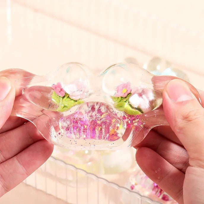 Jucarie Antistres Squishy, Labuta de Pisica Pufoasa cu Revenire Lenta si Insertii Flori, Material TPR Moale, 7 x 6.5 cm, Transparent Multicolor