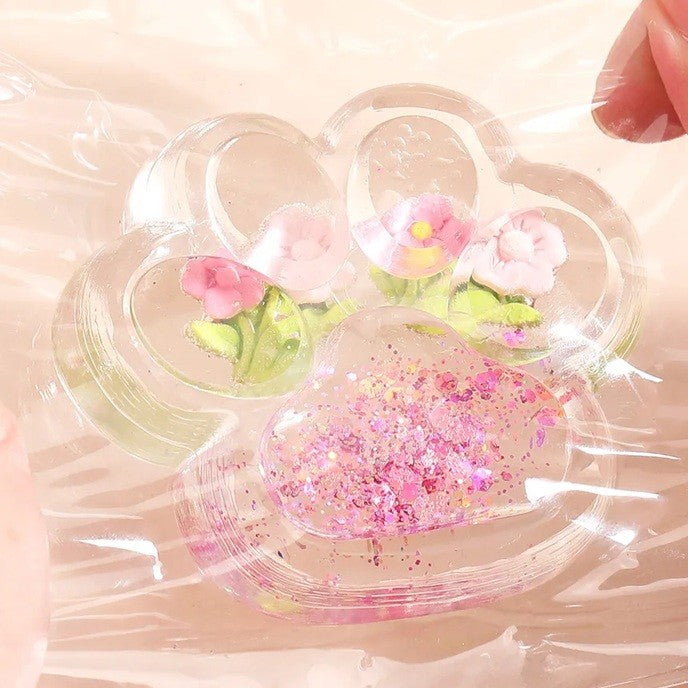 Jucarie Antistres Squishy, Labuta de Pisica Pufoasa cu Revenire Lenta si Insertii Flori, Material TPR Moale, 7 x 6.5 cm, Transparent Multicolor